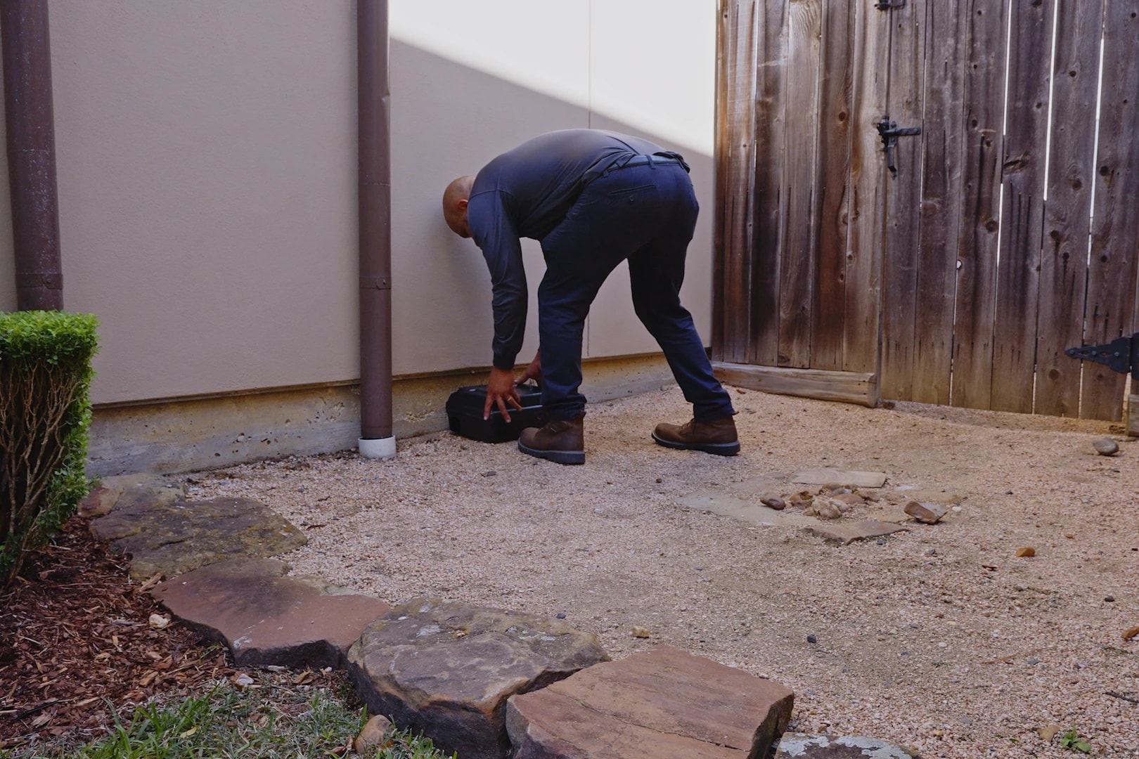 Technician placing a tamper-resistant bait station in a yard corner