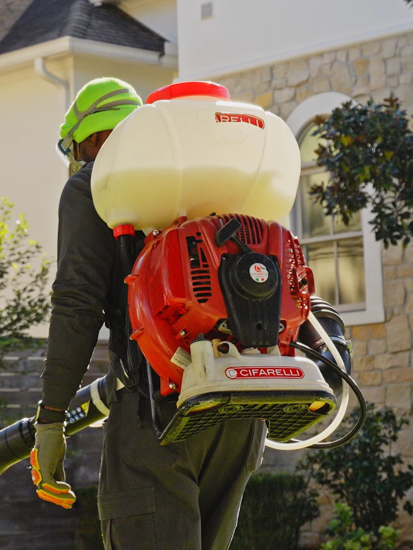 Technician treating a home exterior with a backpack mist blower