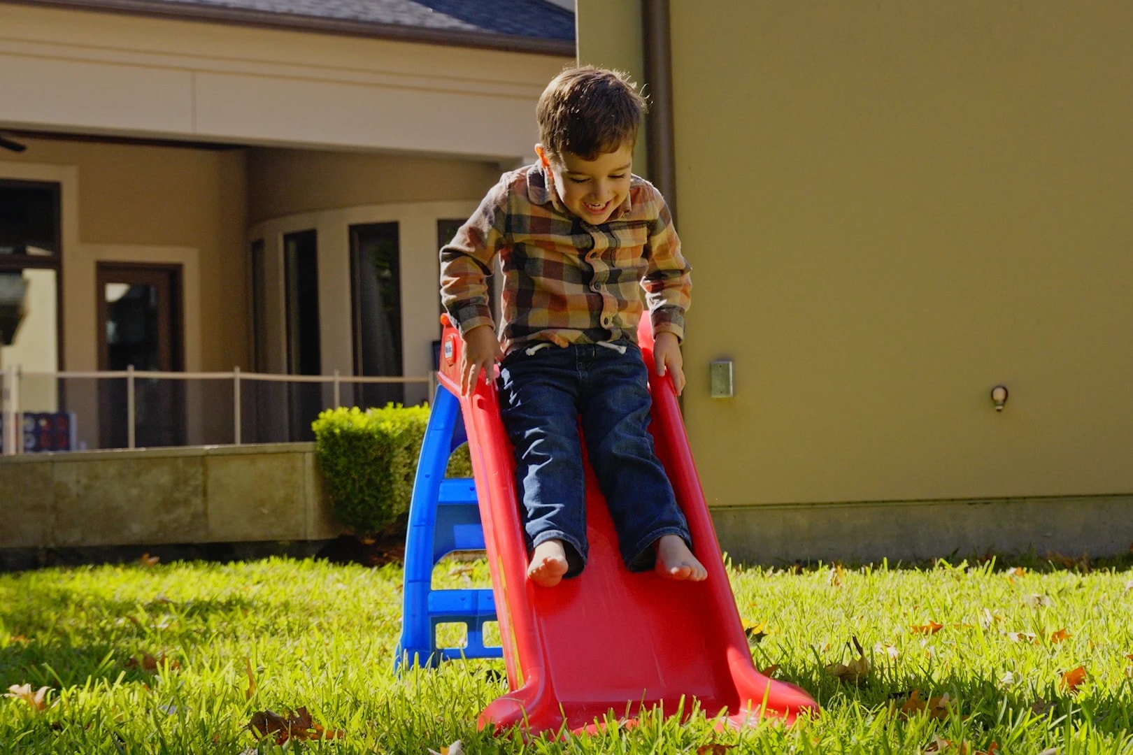 A child playing on a slide in a treated back yard